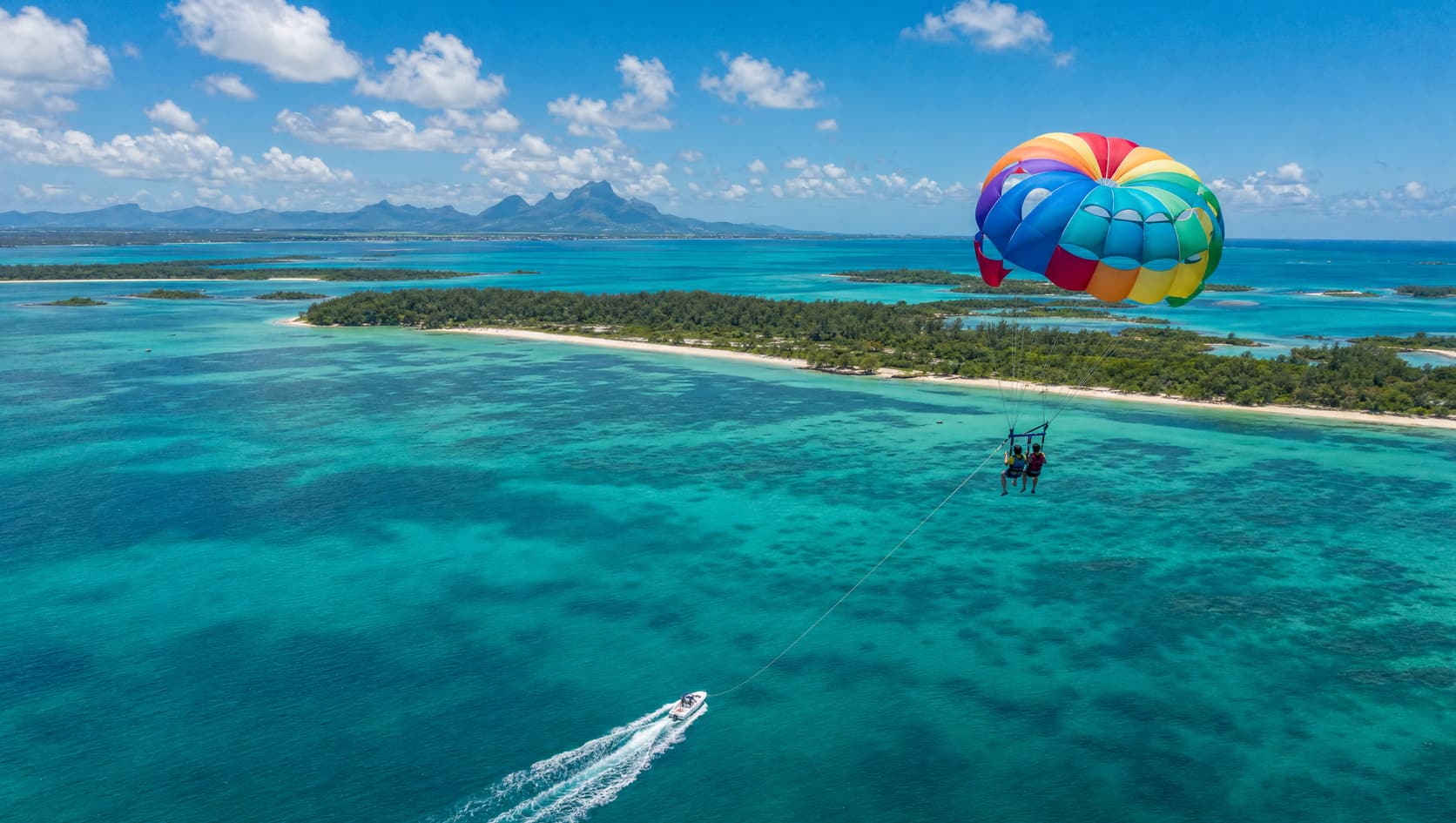 Tandem parasailing high above the turquoise lagoon of Île aux Cerfs, Mauritius, with the towing speedboat below
